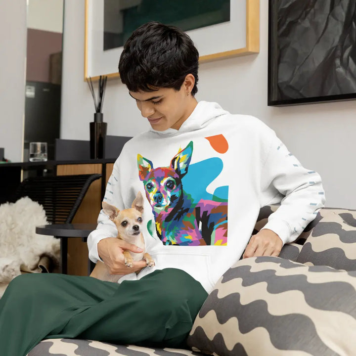 Person wearing a hoodie with a colorful dog design, sitting on a couch holding a small dog.