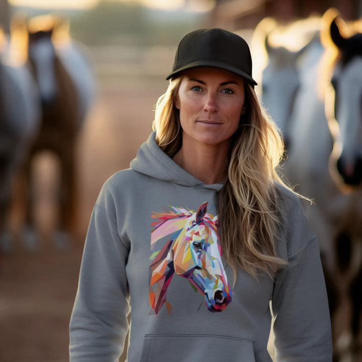 Woman wearing a hoodie with a colorful horse design, standing in front of horses.