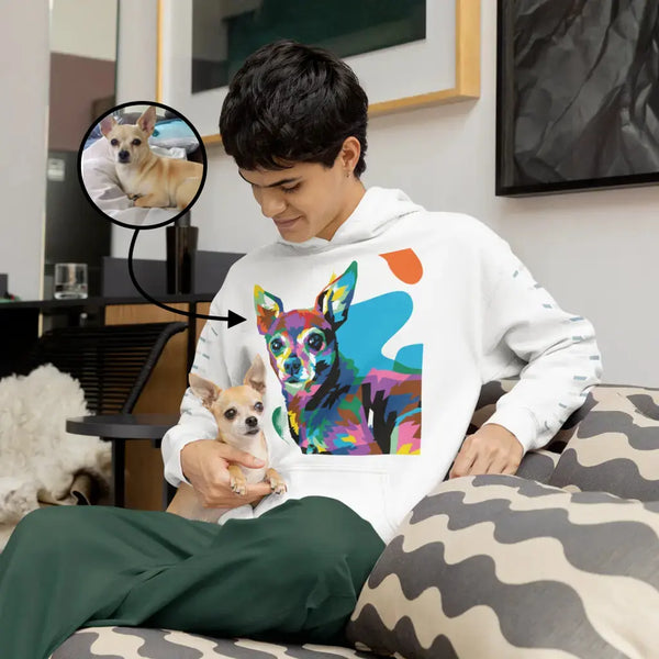 Person wearing a hoodie with a colorful dog design, holding a small dog in a living room.