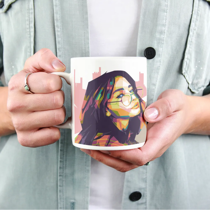 Person holding a mug with a colorful portrait design on a light gray background