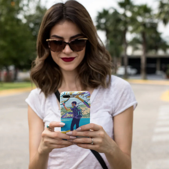 Woman wearing sunglasses and a white shirt, holding a phone with a colorful case.
