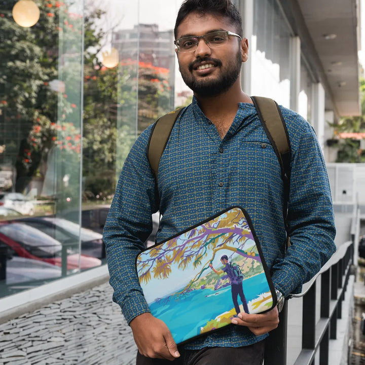 Man holding a colorful laptop case with a scenic design, standing outdoors.