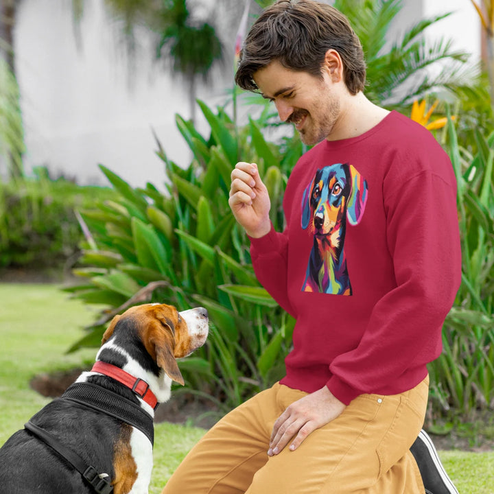 Man in a red sweater with a colorful dog design sitting next to a dog outdoors.