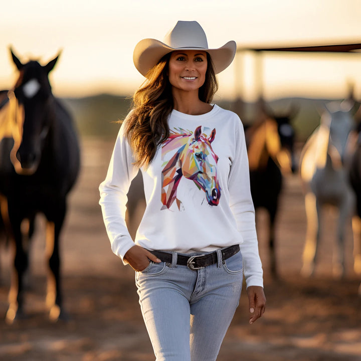 Woman wearing a white sweatshirt with a colorful horse design, standing in front of horses.